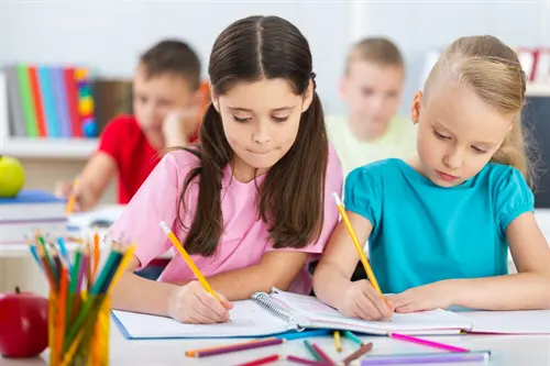 Two girls writing in a classroom with pencils and book